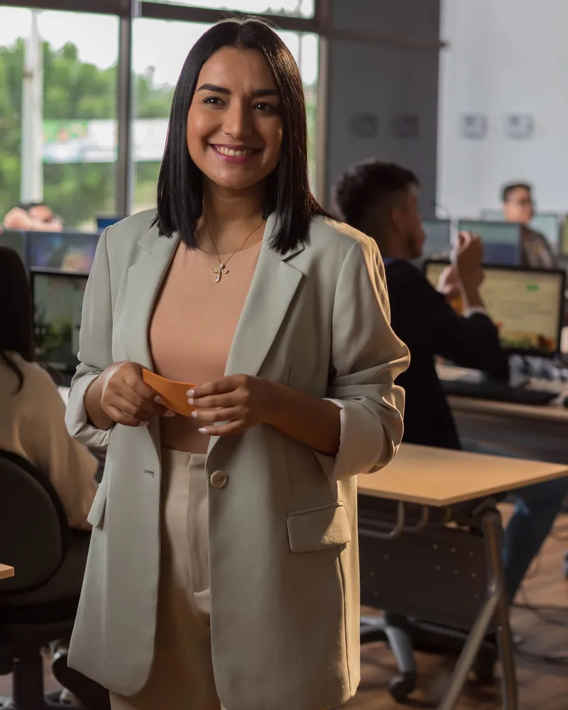 Profesional sonriendo en una oficina, con su equipo trabajando al fondo